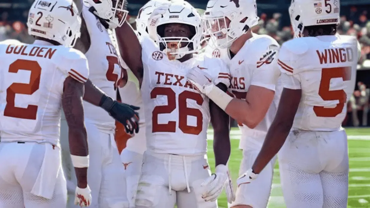A group of Texas Longhorns football players in white uniforms gather and celebrate together on the field during a game.